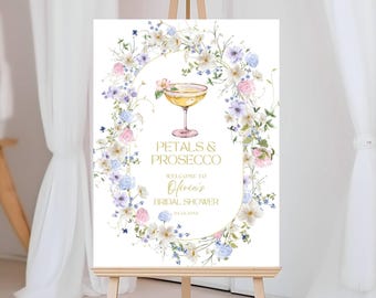 May include: A rectangular sign featuring a watercolor floral wreath in shades of blue, pink, and white surrounding a coupe glass. The text reads PETALS & PROSECCO, WELCOME TO Olivia's BRIDAL SHOWER, and 09.14.202X in gold lettering.