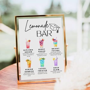 May include: A gold-framed sign with the text "Lemonade BAR" and illustrations of colorful lemonade drinks. Each drink is labeled with a name and ingredients, including "Diploma Dream" and "Berry Proud."