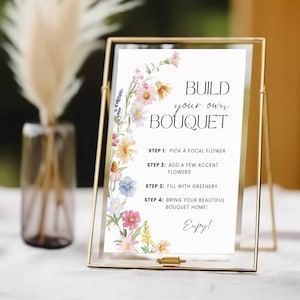 May include: A gold framed sign with the text "BUILD your own BOUQUET" and instructions for creating a bouquet. The sign is decorated with watercolour flowers. A vase with dried flowers is in the background.
