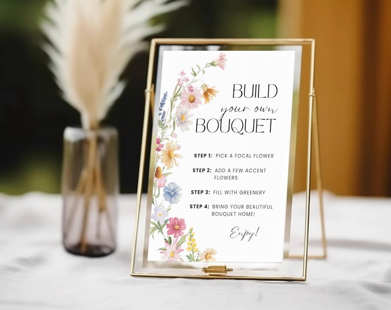 May include: A gold framed sign with the text "BUILD your own BOUQUET" and instructions for creating a bouquet. The sign is decorated with watercolour flowers. A vase with dried flowers is in the background.