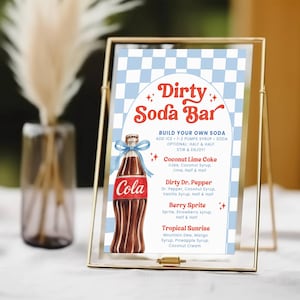 May include: A gold-framed sign for a "Dirty Soda Bar" with a blue and white checkered background. The sign features a cola bottle illustration and a menu with soda recipes like Coconut Lime Coke and Berry Sprite.