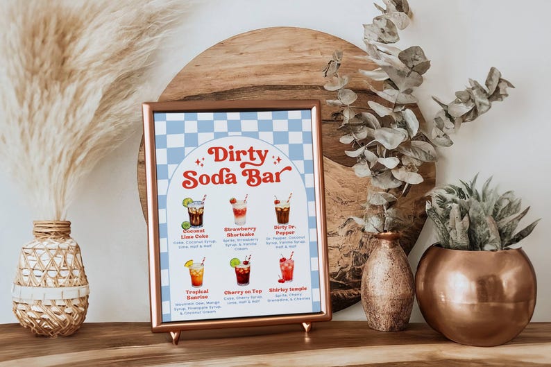 May include: A framed "Dirty Soda Bar" sign with a light blue and white checkered background. The sign features illustrations of six soda drinks with their ingredients listed below. The sign is displayed on a wooden surface.