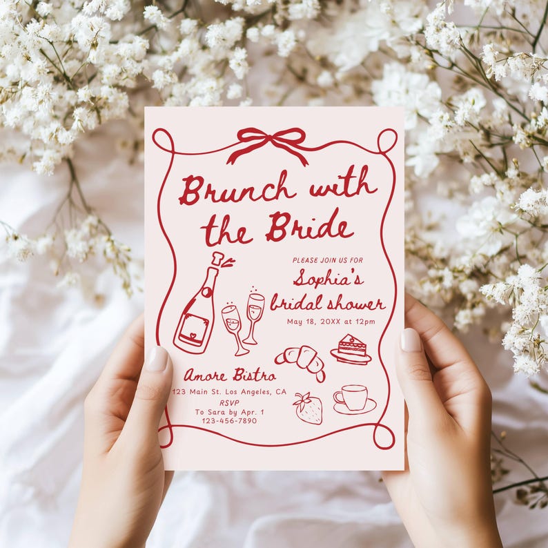 May include: A pink bridal shower invitation with red text and illustrations. The invitation reads "Brunch with the Bride" and includes details for Sophia's bridal shower. The invitation also includes a red ribbon, champagne glasses, a croissant, a slice of cake, a strawberry, and a cup of coffee.