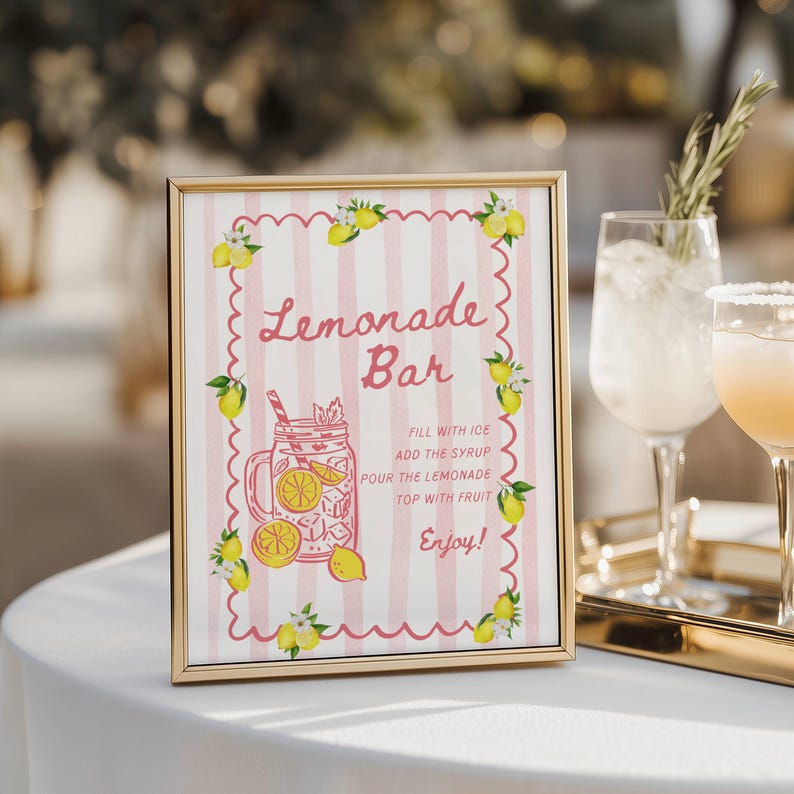 May include: A framed sign with a gold border, featuring a pink and white striped background. The sign reads "Lemonade Bar" in cursive, with a drawing of a lemonade drink and instructions. Yellow lemons and green leaves decorate the edges.