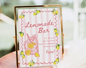 May include: A rectangular sign in a gold frame featuring a pink and white striped background with lemon illustrations and the text: Lemonade Bar, Fill with ice, Add the syrup, Pour the lemonade, Top with fruit, Enjoy! The sign has a scalloped border.