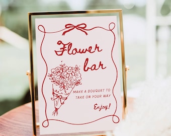 May include: A rectangular sign in a gold metal frame featuring red text and a line drawing of a flower bouquet. The text reads: Flower bar, MAKE A BOUQUET TO TAKE ON YOUR WAY, Enjoy! The sign is enclosed in a decorative red border with a bow at the top.