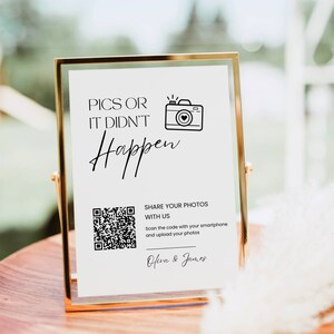 May include: A gold-framed sign with the text "PICS OR IT DIDN'T Happen" and a camera icon. Below is a QR code and the text "SHARE YOUR PHOTOS WITH US". The sign is on a wooden surface.