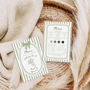 May include: Two invitation cards with green and white striped backgrounds. One card reads "Olivia, Will you be my Maid of Honor?" The other card has wedding details. The cards are on a woven tray with a beige cloth and a feathery plant.