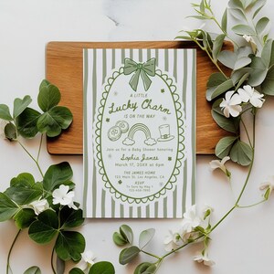 May include: A baby shower invitation with a St. Patrick's Day theme. The invitation features a green and white striped background with a decorative border and the text "A Little Lucky Charm Is On The Way". The invitation includes the name "Sophia James" and event details.