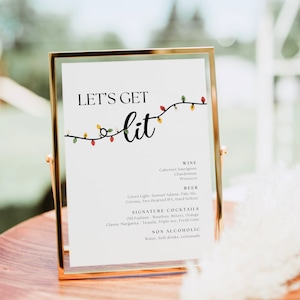 以下が含まれることがあります： 「Let's Get Lit」という黒い文字が書かれた金色の額縁付きの看板。看板には、カラフルなクリスマスライトのストリングが飾られています。看板には、ワイン、ビール、シグネチャーカクテル、ノンアルコールドリンクなど、さまざまなアルコール飲料とノンアルコール飲料の選択肢がリストされています。