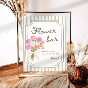 May include: A framed sign with the words "Flower bar" and a watercolor bouquet illustration. The sign has a green and white striped background and includes the text "Make a bouquet to take on your way. Enjoy!"