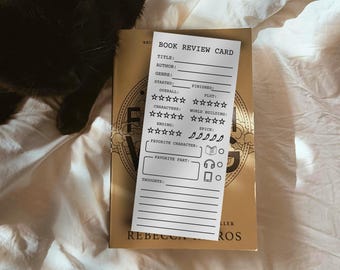 Puede incluir: Una tarjeta de reseña de libros rectangular blanca con texto e iconos negros. La tarjeta incluye campos para título, autor, género, fechas y valoraciones por estrellas para trama, personajes y construcción del mundo.