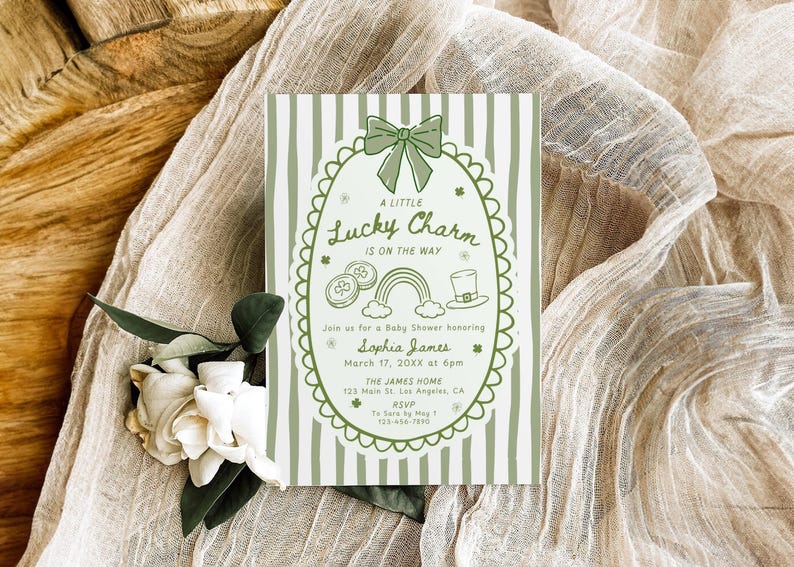 May include: A baby shower invitation with a green and white striped background. The invitation features a green oval frame with a bow, shamrocks, a rainbow, and a leprechaun hat. The text reads "A Little Lucky Charm is on the Way."