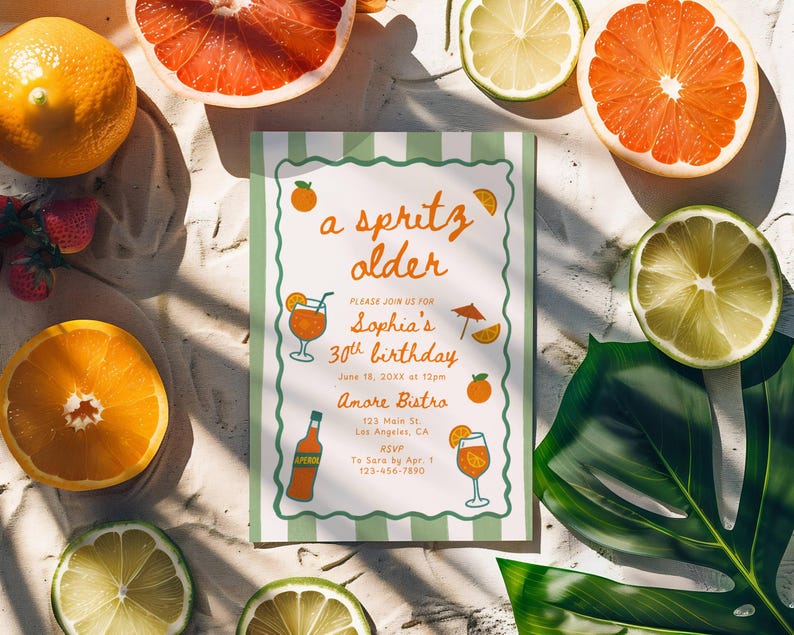 Op de afbeelding: Een verjaardagsuitnodiging met een groen-witte gestreepte rand, met de tekst "a spritz older". De uitnodiging is omgeven door gesneden sinaasappels, grapefruits en limoenen, samen met een groen blad en aardbeien.