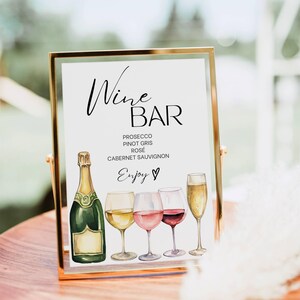 Può includere: Un cartello rettangolare con cornice dorata che presenta il testo Wine Bar, un elenco di vini tra cui Prosecco, Pinot Gris, Rosé e Cabernet Sauvignon, e la parola Enjoy con un'icona a forma di cuore, illustrato con una bottiglia di champagne e quattro calici.