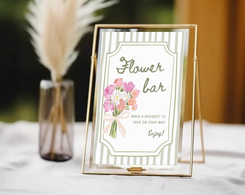 May include: A gold metal framed sign with the words "Flower bar" and a bouquet illustration. The sign includes the text "Make a bouquet to take on your way. Enjoy!" The sign is on a white surface.