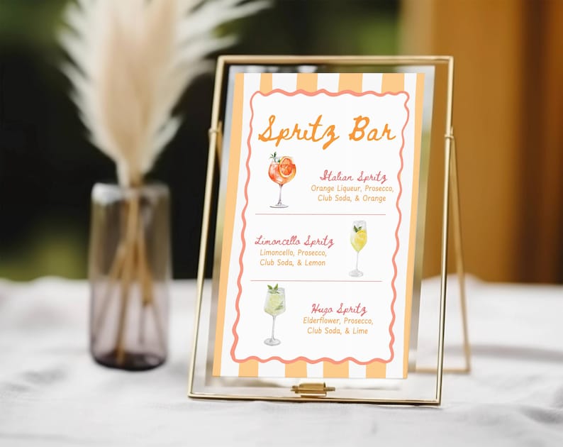 May include: A gold-framed sign with the text "Spritz Bar" in orange script. The sign lists three spritz cocktails: Italian Spritz, Limoncello Spritz, and Hugo Spritz, with watercolor illustrations of each drink.