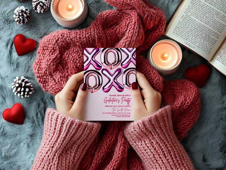 May include: A Valentine's Day party invitation with pink and silver foil balloon letters spelling XOXO is held by a person wearing a pink sweater. The invitation reads "Galentine's Party" with event details. The scene includes candles, hearts, and a cozy pink scarf.