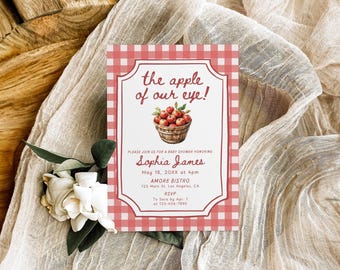 May include: A rectangular baby shower invitation card featuring a red and white gingham border. The text reads: the apple of our eye! Please join us for a baby shower honoring Sophia James May 18, 20XX at 4pm AMORE BISTRO 123 Main St. Los Angeles, CA RSVP To Sara by Apr 1 at 123-456-7890. A watercolor illustration of a basket of red apples is centered.