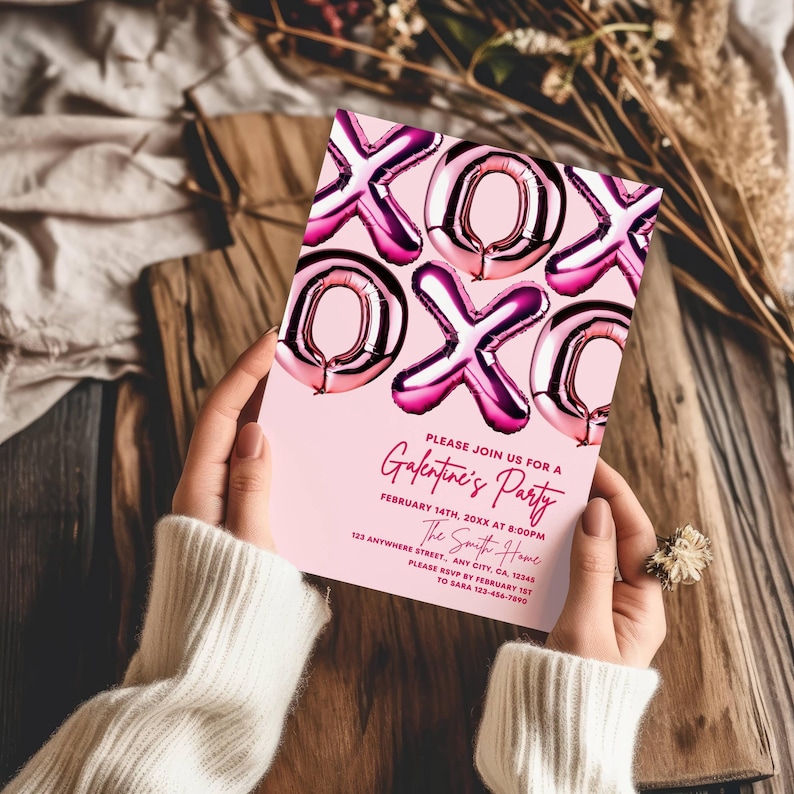 May include: A pink Galentine's Party invitation with foil balloon-style XOXO graphics. The invitation includes event details: date, time, location, and RSVP information. The invitation is held by a person wearing a white sweater.