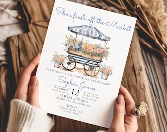 Op de afbeelding: Een witte uitnodigingskaart voor een bruidsdouche met een aquarelillustratie van een blauw-wit gestreepte marktwagen vol kleurrijke bloemen. De tekst luidt: She's fresh off the Market, Sophia James, 12 december om 16:00 uur, Amore Bistro.