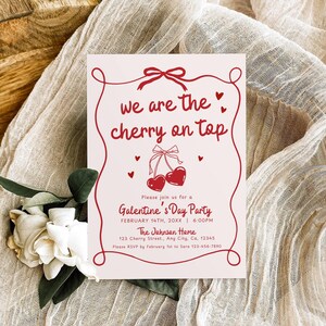 May include: A Valentine's Day party invitation with the text "we are the cherry on top" in red script. The invitation features a cherry design and is on a light pink background. White flowers and fabric are in the background.