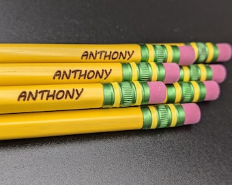 Puede incluir: Un montón de lápices amarillos con detalles verdes y rosas. Cada lápiz está grabado con el nombre "ANTHONY".