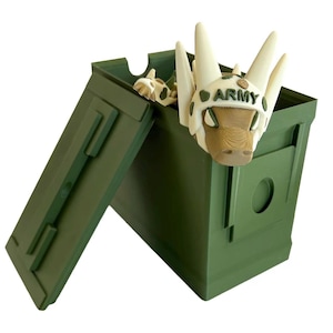 May include: A green metal ammo can with the lid open. Inside the can is a white and green camouflage toy with a brown face and the word "ARMY" on its head.