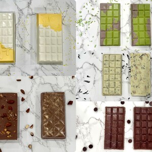 May include: Assortment of chocolate bars with different toppings and flavors.  The bars are arranged in a grid pattern on a white marble surface.  The toppings include almonds, sprinkles, and tea leaves.