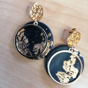 Könnte beinhalten: Ein Paar goldene und schwarze Ohrringe mit einem runden, strukturierten goldenen Oberteil und einem schwarzen Kreis mit goldenen Flecken. Der schwarze Kreis hat einen goldenen Ring darum.