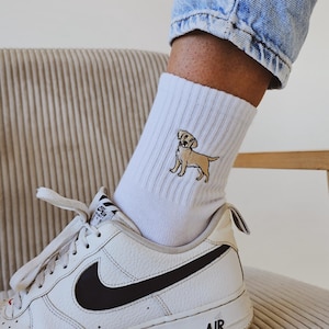 May include: White socks with an embroidered yellow labrador retriever on the side. The socks are worn with white trainers with a black swoosh and the word "AIR" on the side.