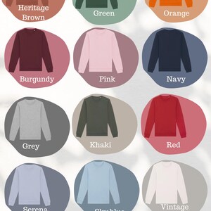 May include: A color palette graphic featuring various crewneck sweatshirts in a range of colors, including Heritage Brown, Green, Orange, Burgundy, Pink, Navy, Grey, Khaki, Red, Serena Blue, Sky Blue, Vintage White, White, Black, and Desert Dust. The text "Colour Palette" is at the top.