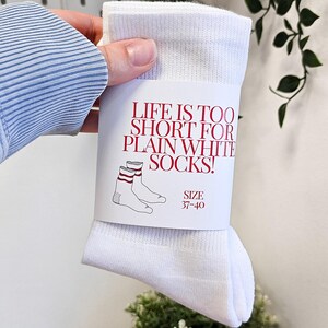 Peut inclure: Des chaussettes blanches avec des rayures rouges et blanches. L'emballage indique "La vie est trop courte pour les chaussettes blanches simples !" et "Taille 37-40".