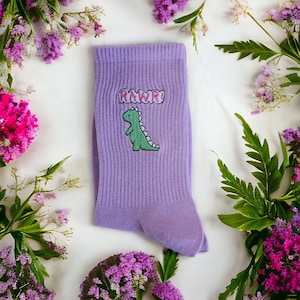 以下が含まれることがあります： 緑色の恐竜と「RAWR！」という刺繍が施された紫色の靴下です。
