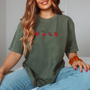 May include: A green t-shirt with a graphic of strawberries, cherries, a watermelon slice, and a pineapple. The shirt is made of a soft, comfortable material and has a relaxed fit.