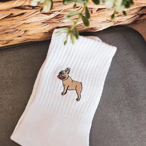 May include: White cotton socks with an embroidered image of a French bulldog. The dog is brown with a black nose and a red tongue.