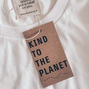 May include: White t-shirt with a brown tag that says "Kind to the Planet". The tag is attached to the shirt with a white string. The shirt also has a smaller tag that says "Don't let anyone put a label on you. www.duskshop.it"