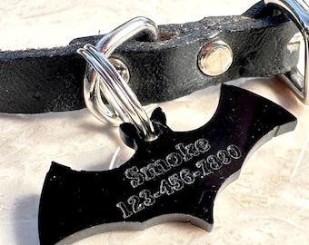 Puede incluir: Collar de perro de cuero negro con una etiqueta de metal en forma de murciélago plateada que dice "Smoke 123-456-7800".
