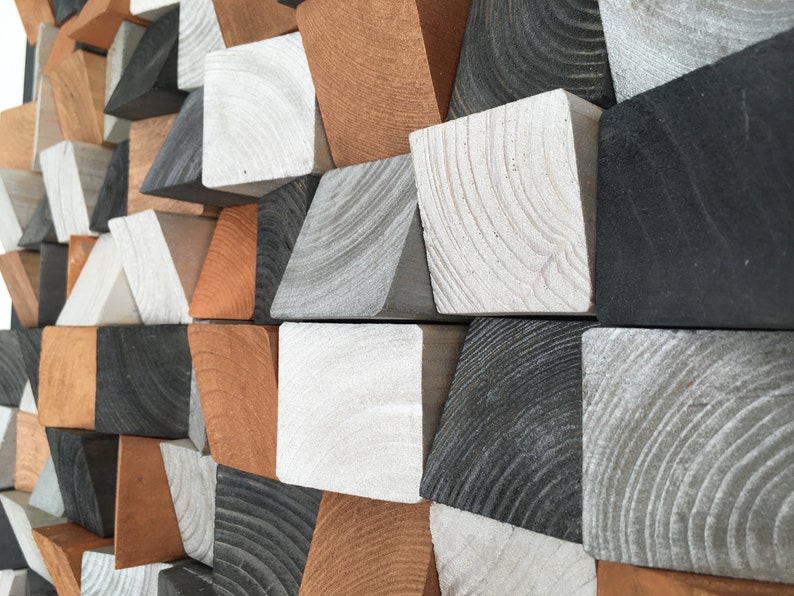 May include: A geometric wall art piece made of wood blocks in various shades of brown, gray, and black. The blocks are arranged in a staggered pattern, creating a visually interesting and modern design.