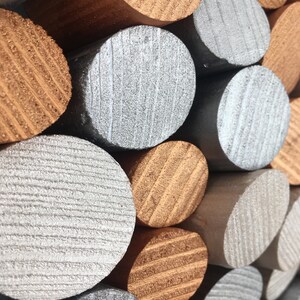 May include: A close-up of a stack of wooden dowels painted in silver and copper. The dowels are arranged in a staggered pattern, creating a textured and visually appealing design.