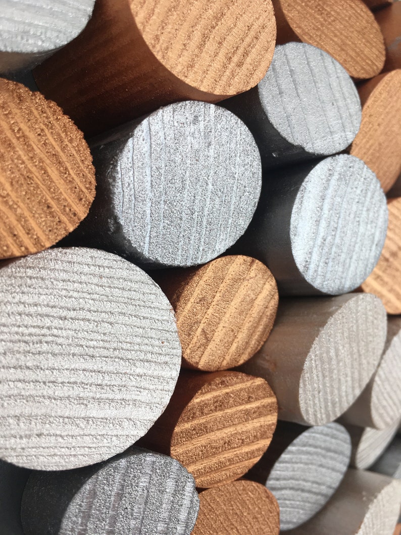 May include: A close-up of a stack of wooden dowels painted in silver and copper. The dowels are arranged in a staggered pattern, creating a textured and visually appealing design.