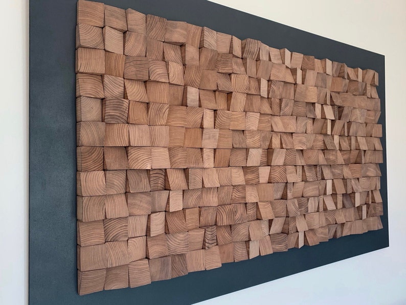 Puede incluir: Una gran pieza de arte de pared hecha de bloques de madera de varios tama&ntilde;os y formas. Los bloques est&aacute;n dispuestos en un patr&oacute;n de onda y son de color marr&oacute;n claro. La pieza est&aacute; montada sobre un fondo gris oscuro.