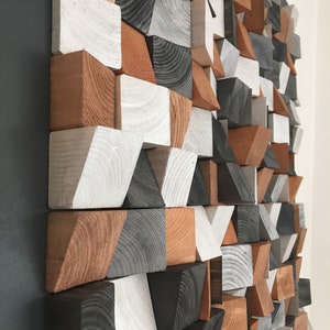 May include: A geometric wall art piece made of wood blocks in various shapes and sizes. The blocks are painted in shades of white, gray, and brown.