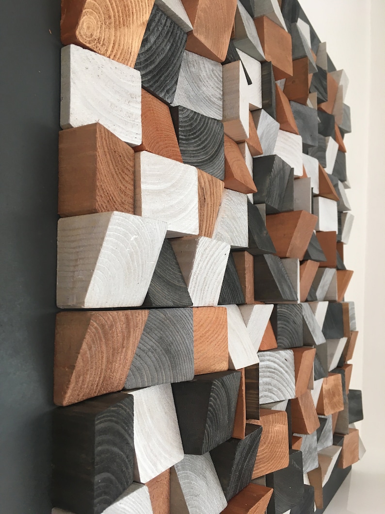 May include: A geometric wall art piece made of wood blocks in various shapes and sizes. The blocks are painted in shades of white, gray, and brown.