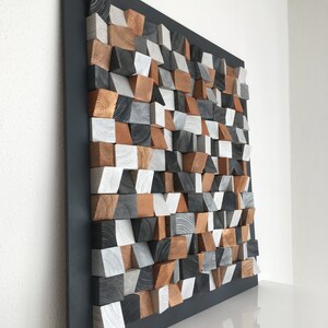 May include: A wall sculpture made of wood blocks in various shades of brown, gray, and white. The blocks are arranged in a geometric pattern and are mounted on a black background.