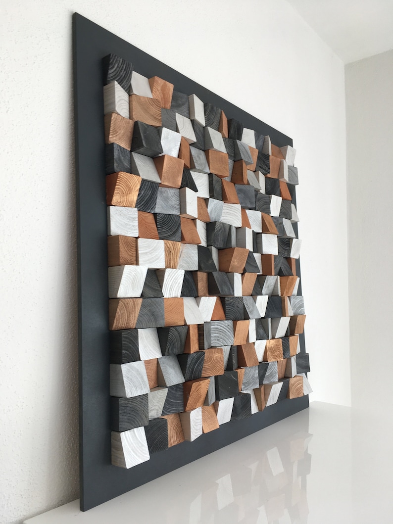 May include: A wall sculpture made of wood blocks in various shades of brown, gray, and white. The blocks are arranged in a geometric pattern and are mounted on a black background.