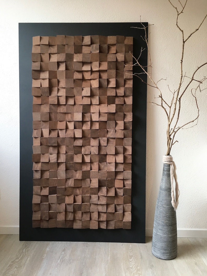 Puede incluir: Una gran pieza de arte de pared de madera hecha de muchos cuadrados peque&ntilde;os, dispuestos en un patr&oacute;n geom&eacute;trico. Los cuadrados son de color marr&oacute;n oscuro y tienen una veta de madera natural. El arte de pared est&aacute; enmarcado en un marco negro y est&aacute; colgado en una pared blanca. Un jarr&oacute;n con una rama seca est&aacute; en primer plano.