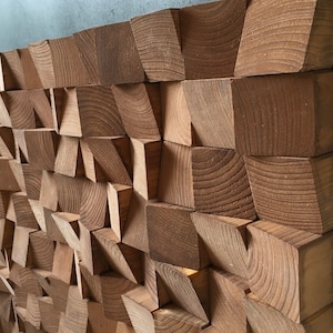 Puede incluir: Una pieza de arte de pared hecha de bloques de madera en varias formas y tama&ntilde;os. Los bloques est&aacute;n dispuestos en un patr&oacute;n geom&eacute;trico, creando un aspecto texturizado y moderno. La madera es de color marr&oacute;n natural.
