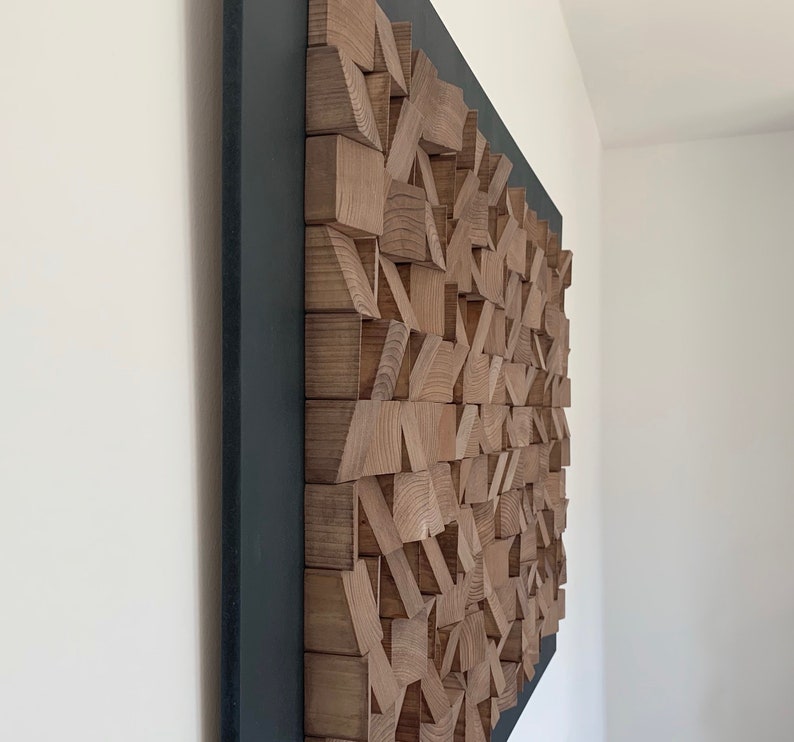 Puede incluir: Una escultura de pared hecha de bloques de madera de varios tama&ntilde;os y formas, dispuestos en un patr&oacute;n geom&eacute;trico. La escultura est&aacute; montada en un marco negro y tiene un acabado de madera natural.