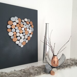 May include: A black canvas with a heart shape made of silver and copper colored circles. A silver vase with a branch of twigs is on a white surface with a gray fur rug. A copper vase with a branch of twigs is on a silver tray with two gray and copper colored circles.